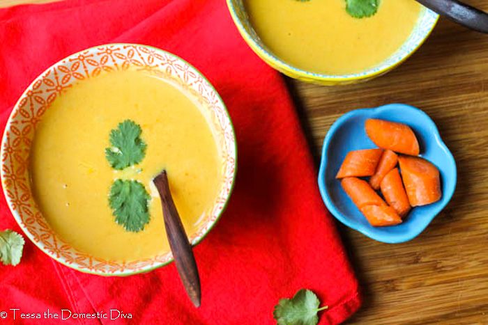 birds eye view of two colorful bowls filled with a creamy carrot soup with cilantro garnish atop a red cloth