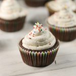 chocolate cupcakes topped with a white buttercream frosting baked in colorful rainbow papers on a whitewashed wooden surface