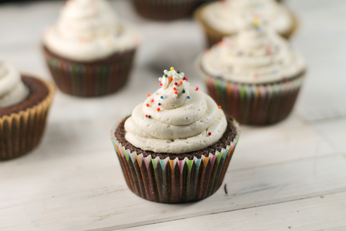 chocolate cupcakes topped with a white buttercream frosting baked in colorful rainbow papers on a whitewashed wooden surface