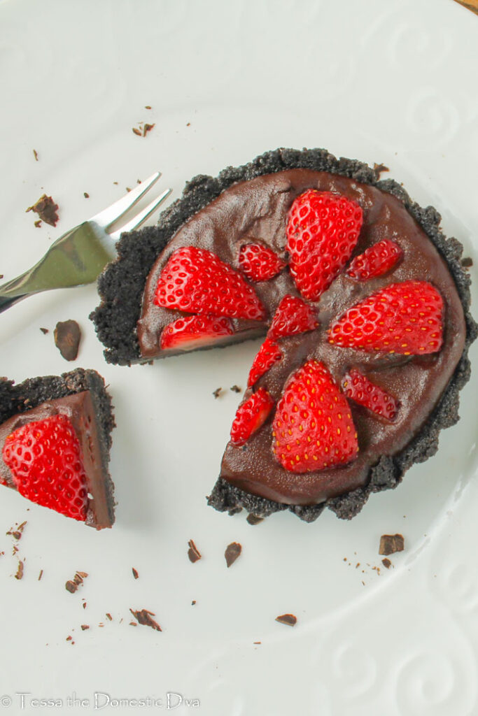 a fluted cookie crust tart with a chocolate ganache and halved fresh strawberries pressed into the top