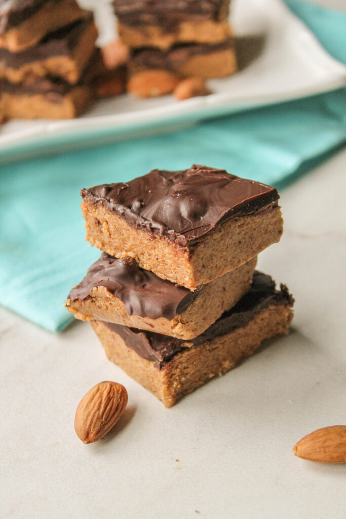 three chocolate covered protein bars in a stack on a marble surface.