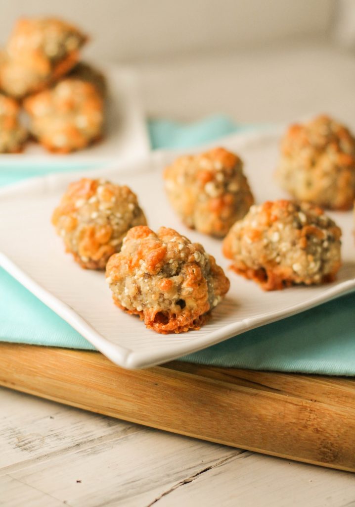 vertical image of paleo sausage cheese balls on a white plate, turquoise cloth, and bamboo cutting board