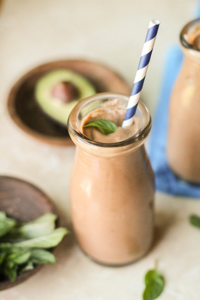 old fashion milk glass filled with a thick and creamy chocolate shake with a mint leaf garnish and a blue and white striped paper straw