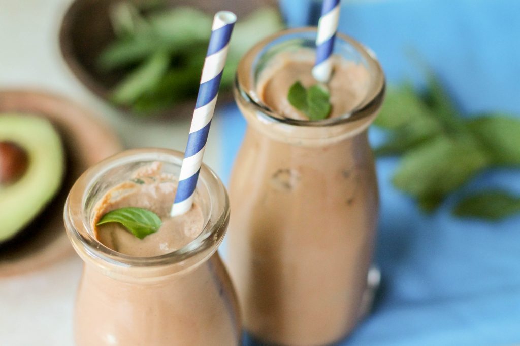 a thick and creamy keto chocolate milkshake on a royal blue cloth with a white a blue striped paper straw and a mint leaf garnish