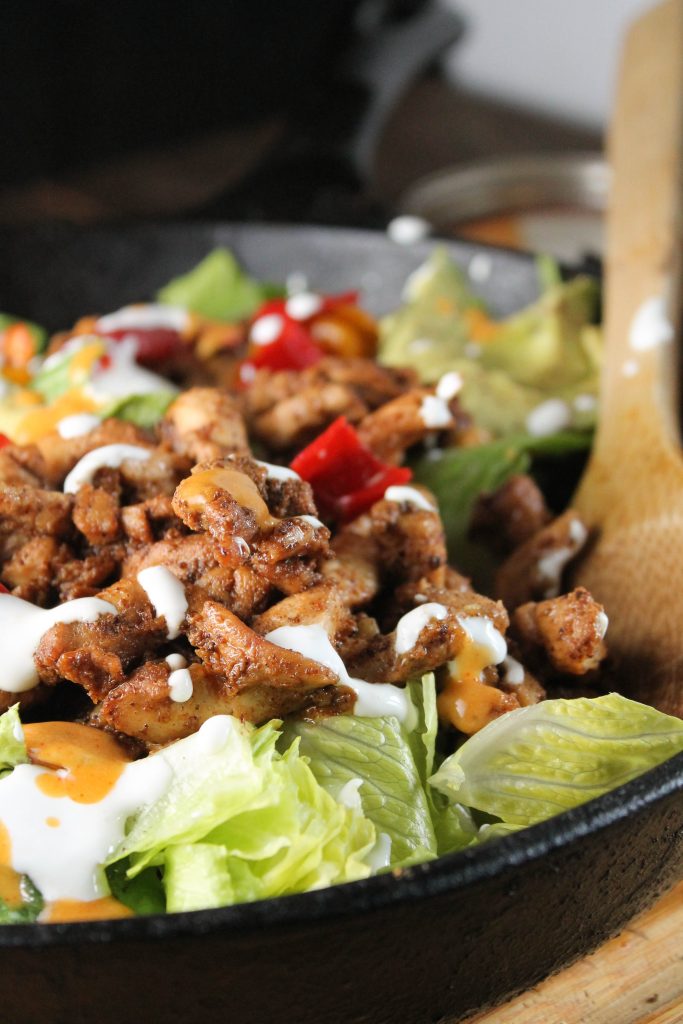 vertical image of well seasoned chicken fajitas topped with a drizzle of crema in a cast iron pan with wooden serving spoon