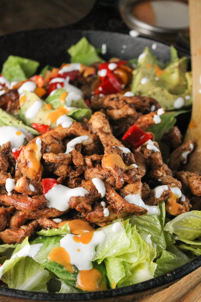 a front view close up of a cast iron skillet with fresh chicken fajitas topped with sour cream atop a bed of fresh romaine