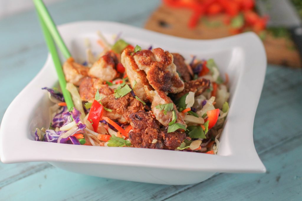 Paleo Sesame Chicken served on chopped carrots and cabbage in a white bowl 