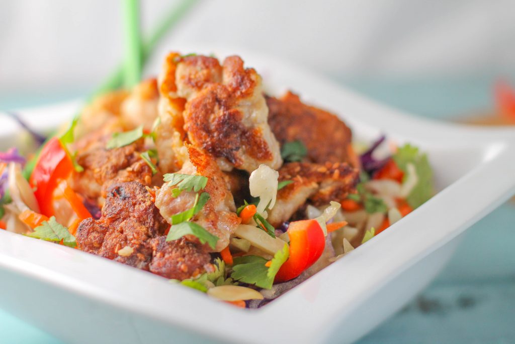 Side view of Paleo Sesame Chicken served on chopped carrots and cabbage in a white bowl 