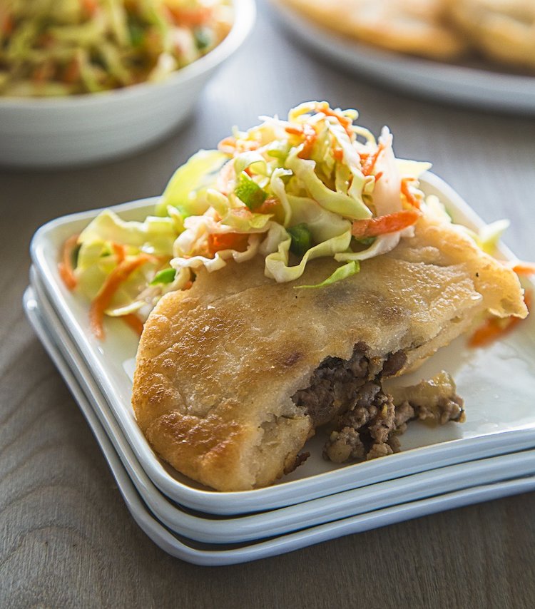 a meat filled pastry topped with a fresh cabbage slaw on white plate