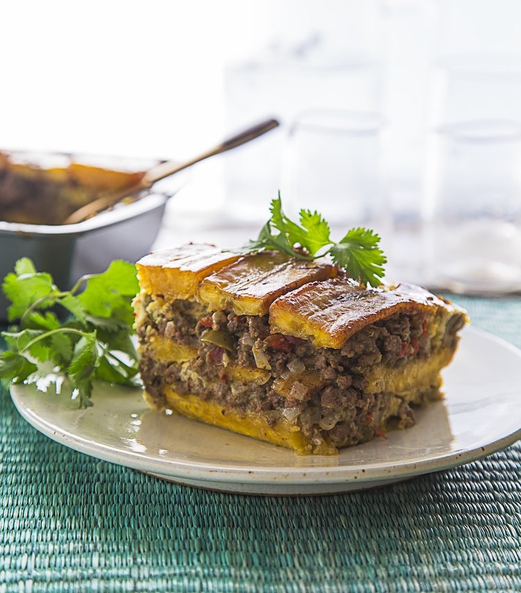 a vertical image of a layered sauteed plantain and ground beef casserole on a white plate 