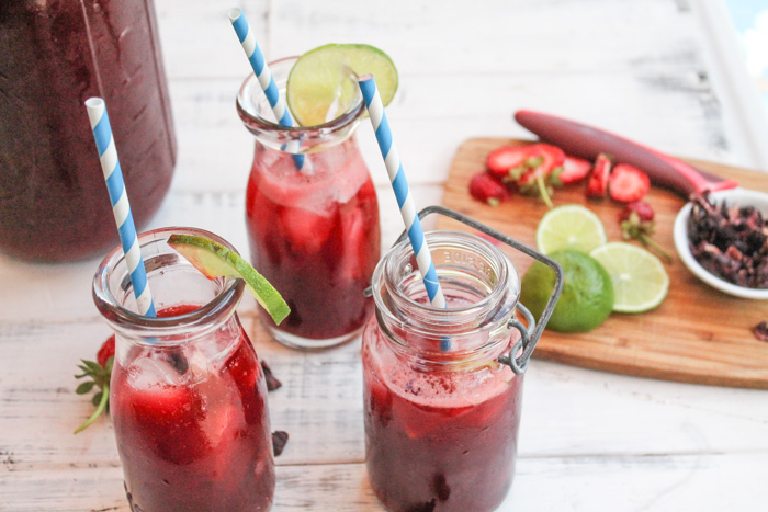 three clear glasses of red hibiscus sweet tea with lime and strawberry