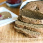 horizontal image of a sliced loaf of a dark brown low carb bread loaf with fresh jelly in a turquoise dipping dish in the background