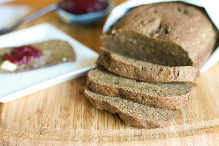 horizontal image of a sliced loaf of a dark brown low carb bread loaf with fresh jelly in a turquoise dipping dish in the background