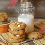 vertical image of 4 stacked pumpkin cookies with a vintage milk jar and fall themed linen