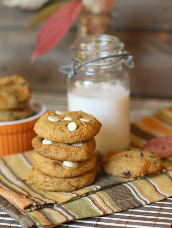 4 stacked pumpkin cookies with a vintage milk jar and fall themed linen