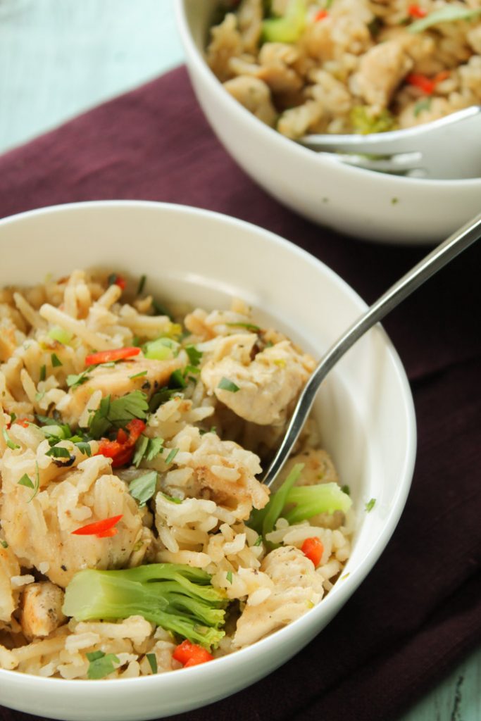 vertical image of two white bowls on a plum colored linene filled with golden hued basmati rice. broccoli, and chicken chinks garnished with some finely chopped red pepper