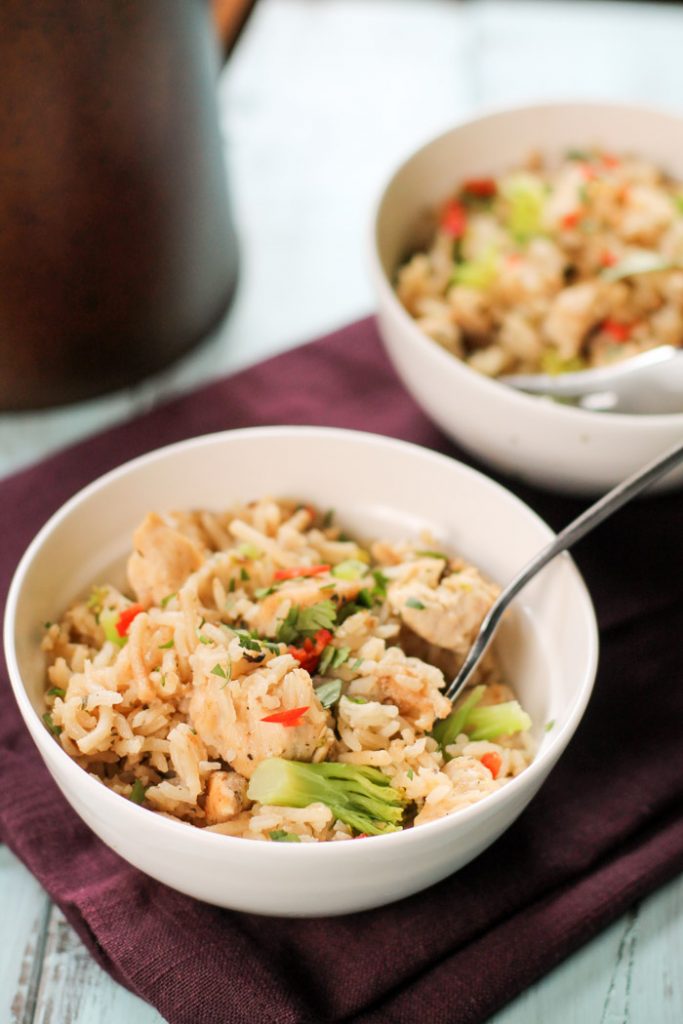  two white bowl atop a plum colored linen filled with chicken, rice, and vegetables