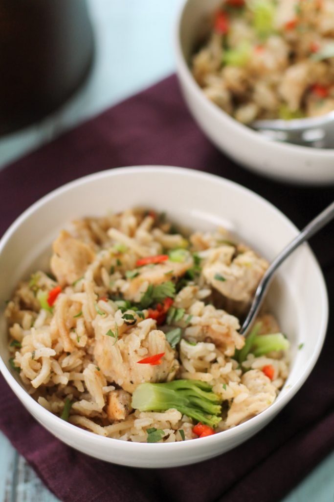 a white bowl filled with chicken and rice and garnished with vegetables 