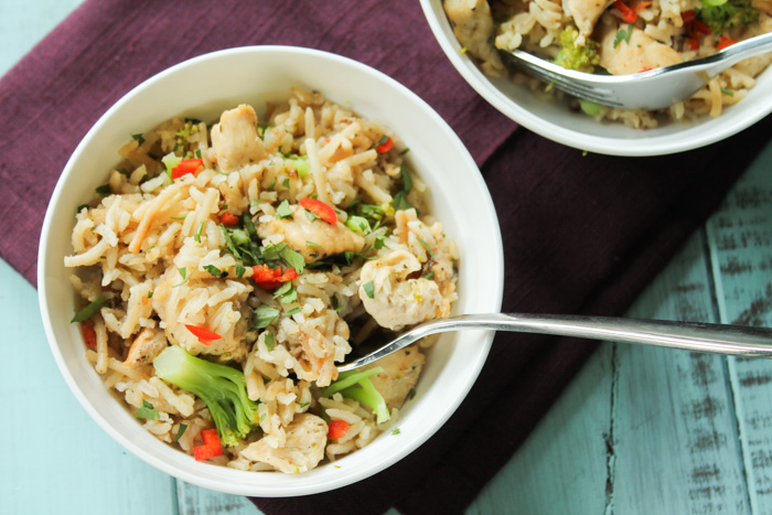 overhead of two white bowls filled with chicken flavored rice, bonelss chicken, and broccoli on plum colored linen