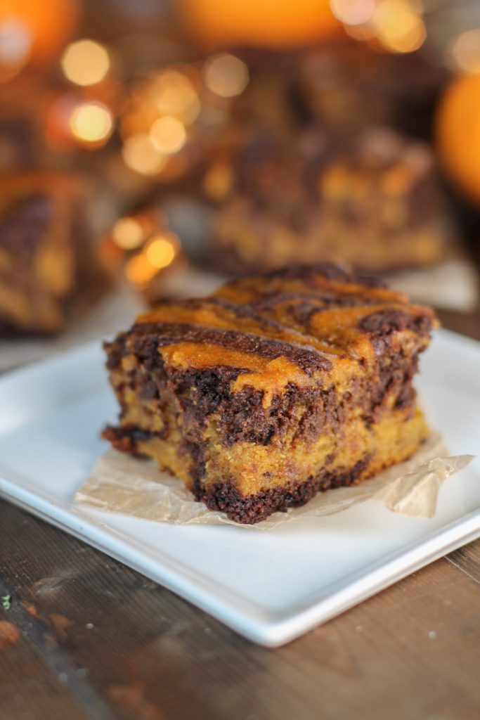 chocolate swirled pumpkin brownie with amber hued lights in background on a dark wooden surface