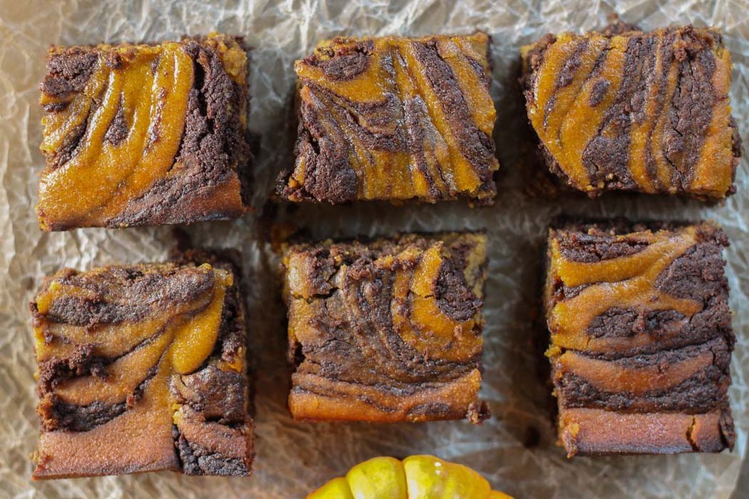 pumpkin and chocolate swirled brownies in two rows with a crumbled natural piece of parchment underneath