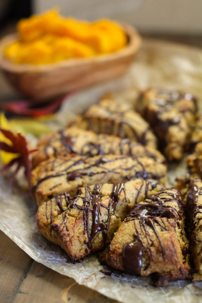 triangular pumpkin scones witha chocolate drizzle arranged in a circle with an olive wood bowl of pumpkin puree in background.