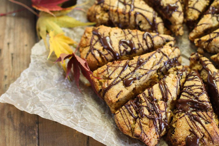 horizontal image of chocoalte drizzled pumpkin scones from overhead atop a crumpled parchment paper and fall leaves scattered about