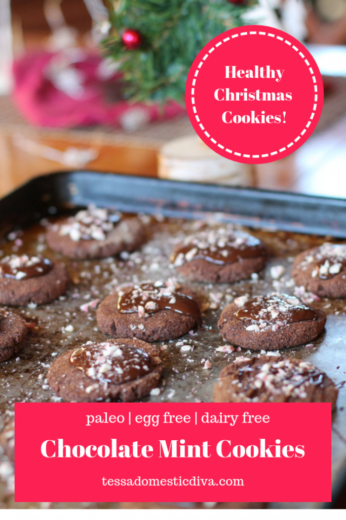 pinterest ready cookie sheet filled with chocolate cookies topped with melty ganache and crushed candy canes with a Christmas tree in the background