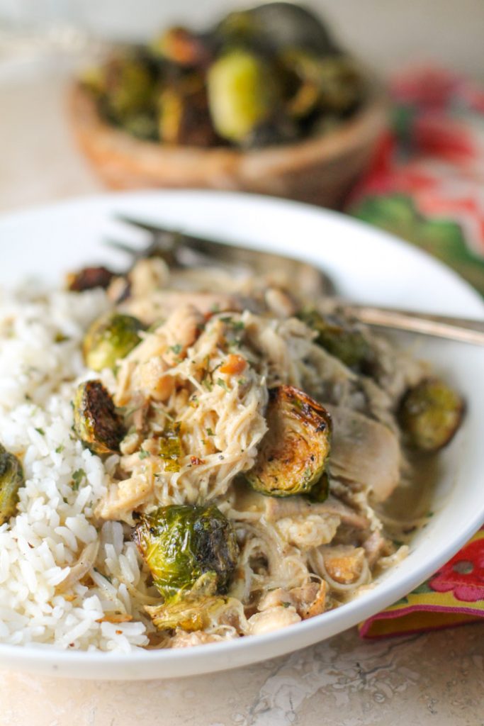 a white pasta bowl on tender shredded chicken and roasted brussel sprouts in a white bowl with a tarnished silver fork