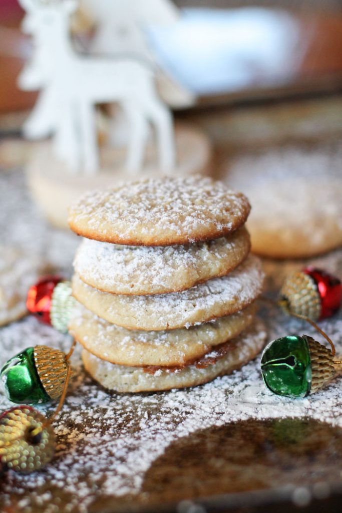 vertical image of 5 stacked cheesecake cookies sprinkled with powdered sugar and red and green ornament garland woven through