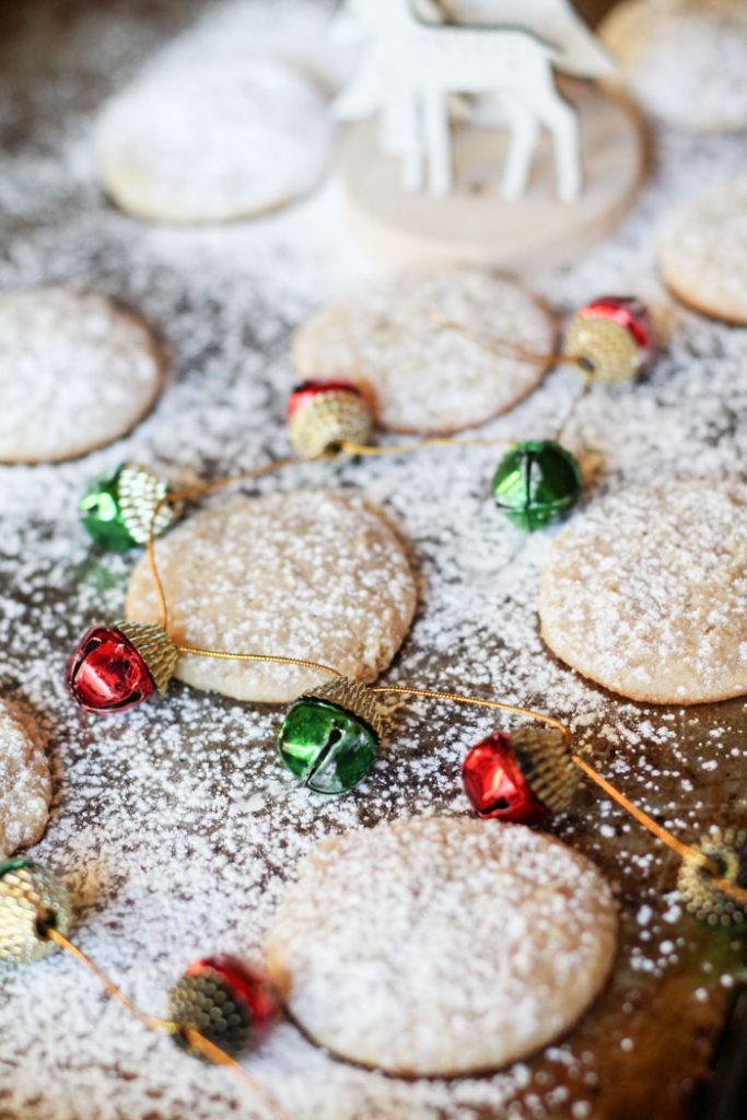 vertical image of powdered sugar dusted cheescake cookies on a cookie sheet with a garland of red and green ornaments winding around