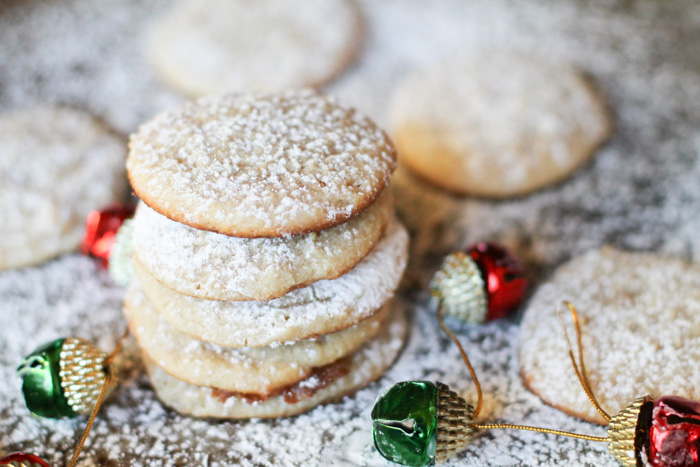 horizontal image of 5 stacked cheesecake cookies sprinkled with powdered auagr on a cookie sheet with a garlnad of red and green ornaments scattered about