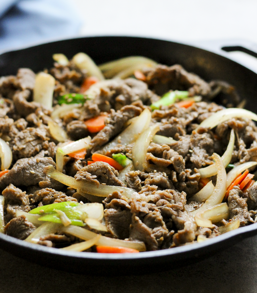 eye level shot of a cast iron pan filled with thinly sliced and cooked beef, onions, and peppers