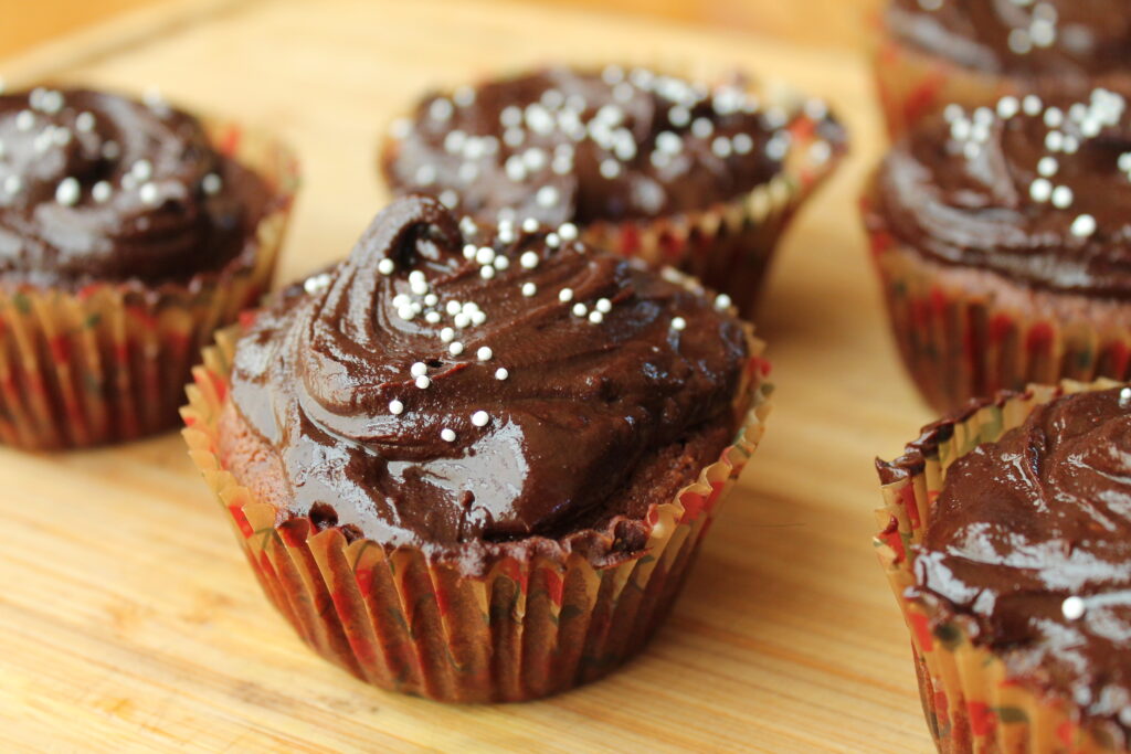 chocoalte glazed chocoalte cupcakes in paper liners atop a wooden cutting board