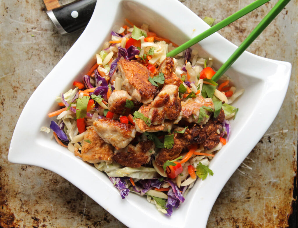 overhead view of a bowl of Chinese sesame chicken atop a Chinese slaw