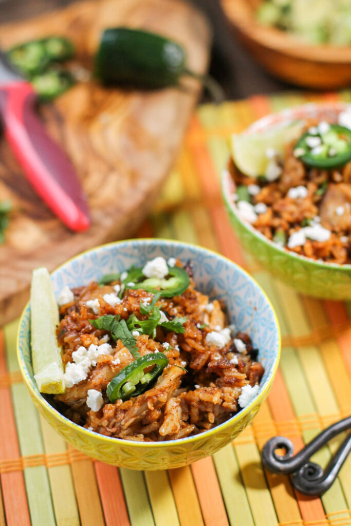 two bowls filled with arroz con pollo and topped with lime, cilantro, and jalapenos