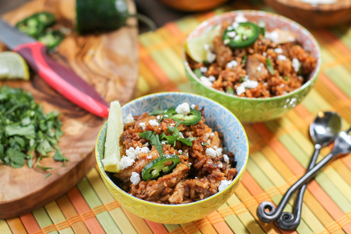 horizontal image from above of two colorful bowls filled with a tomato rice and tender chicken shreds topped with cilantro, feta cheese, and jalapeños