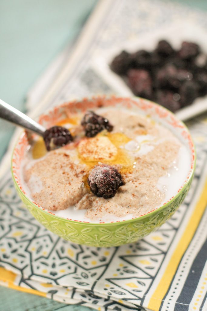 a lime green patterned bowl filled with a creamy hot cereal topped with melting butter, a sprinkle of cinnamon, a touch of cream and fresh blackberries