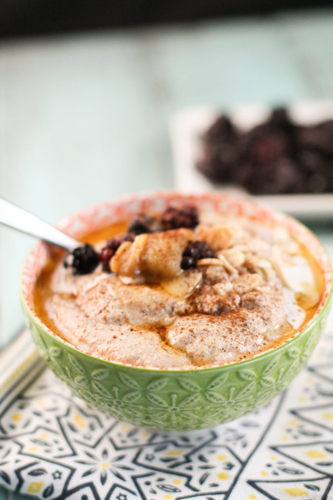 a lime green bowl filled with a creamy nut and seed porridge topped with sliced almonds, berries, and butter