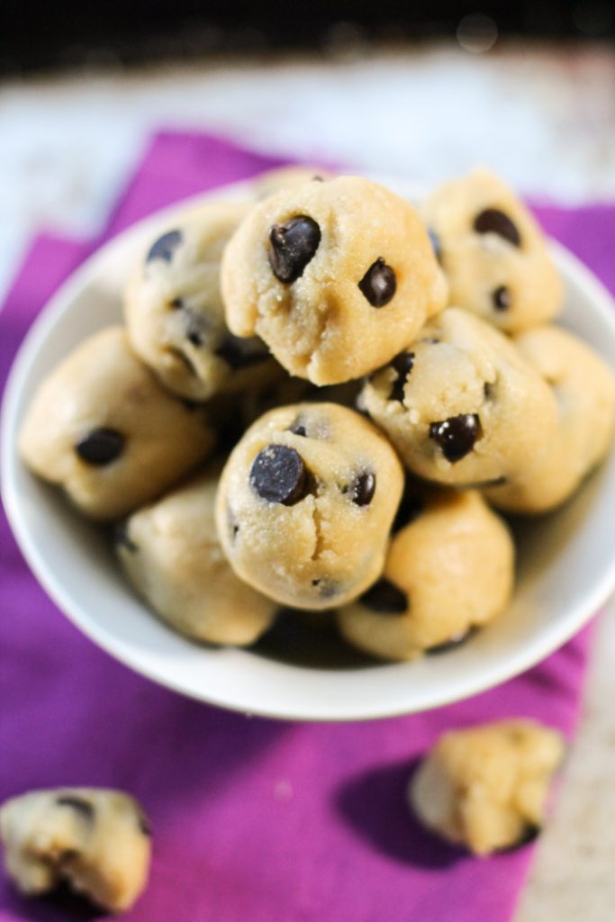 no bake cookie dough balls studded with chocolate chips from above on top of a bright purple cloth and weathered cookie sheet