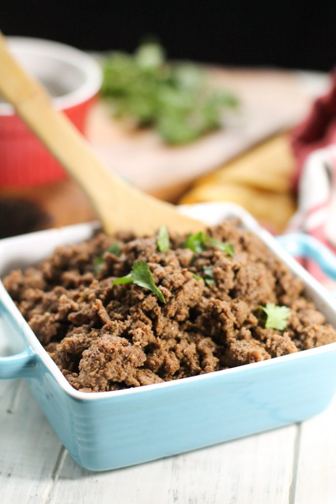 Seasoned ground beef in a turquoise and white ceramic dish with chopped cilantro and Mexican spice in the background.