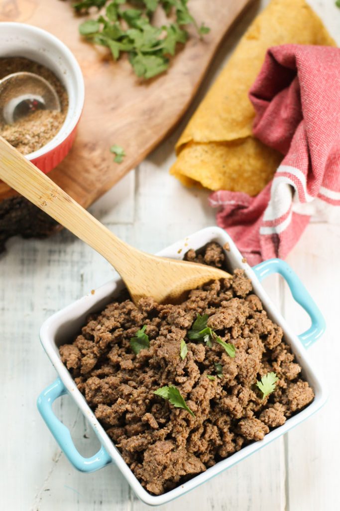 birds eye view of a square baking dish filled with seasoned ground beef for tacos with spices and a rolled tortilla