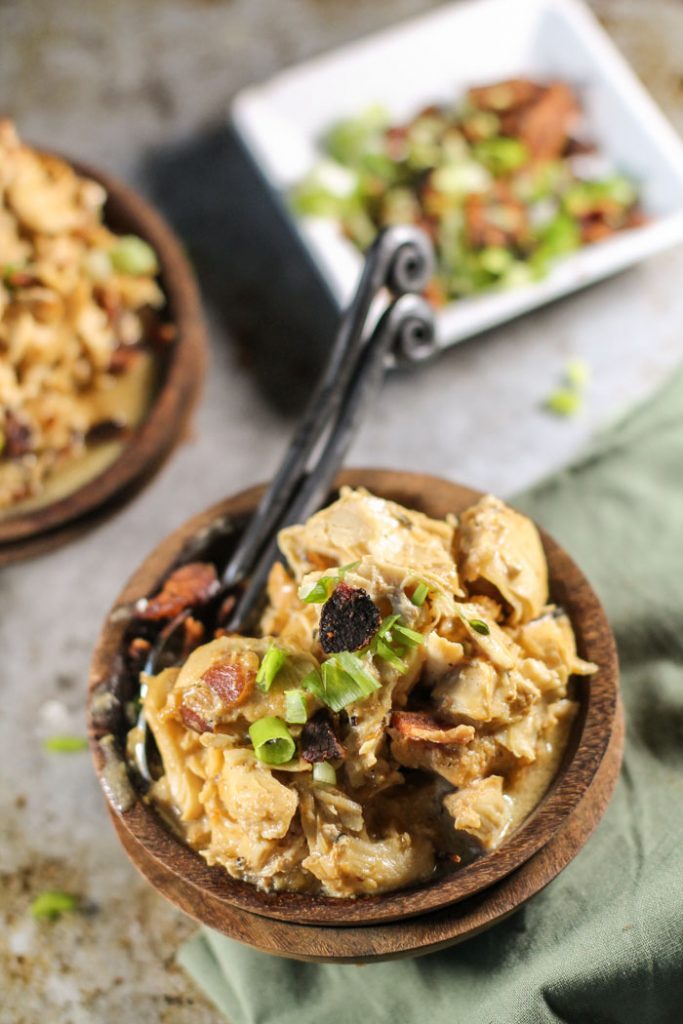 overhead shot of two dark wooden pulls filled with shredded chicken thighs in a creamy sauce and topped with chopped bacon