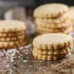 stacked circle shaped sugar cookies atop a weathered cookie sheet with holiday cookie cutters