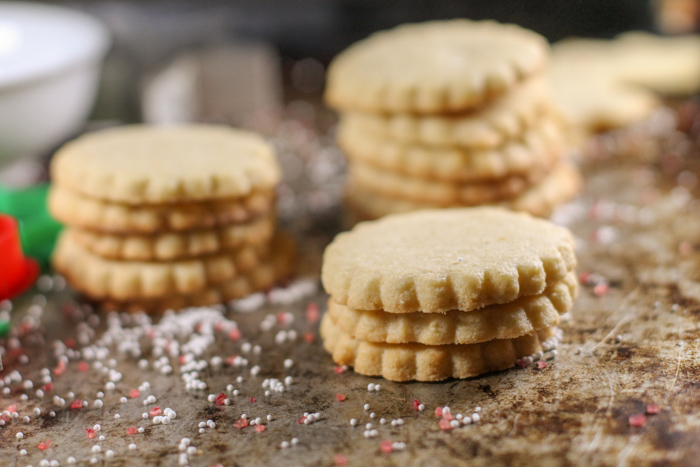 stacked circle shaped sugar cookies atop a weathered cookie sheet with holiday cookie cutters