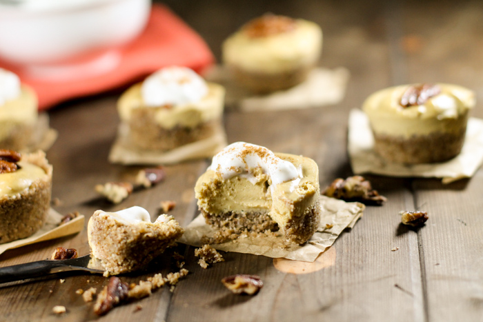 mini no bake pumpkin cheesecake tarts topped with whipped cream and arranged on a dark wooden surface