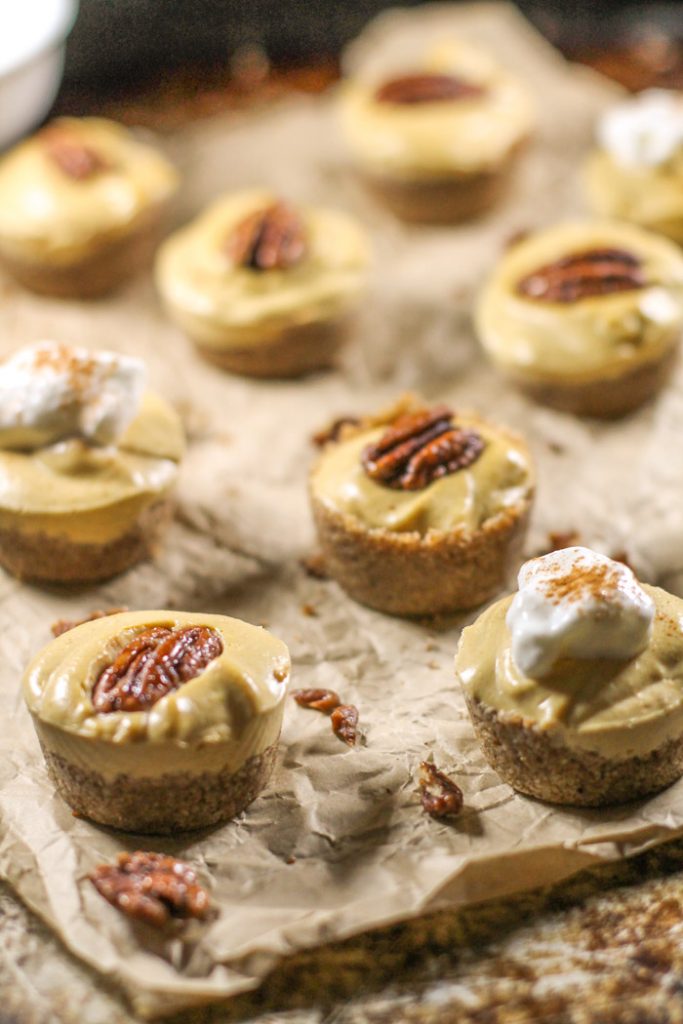 mini pumpkin cheesecake tarts topped with a candied pecan arranged on crumpled piece of brow parchment paper atop an antiqued cookie sheet