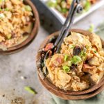 birdseye view of two dark wooden bowls filled with pulled chicken in a creamy sauce with bacon and a scallion garnish