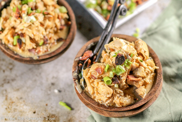 birdseye view of two dark wooden bowls filled with pulled chicken in a creamy sauce with bacon and a scallion garnish