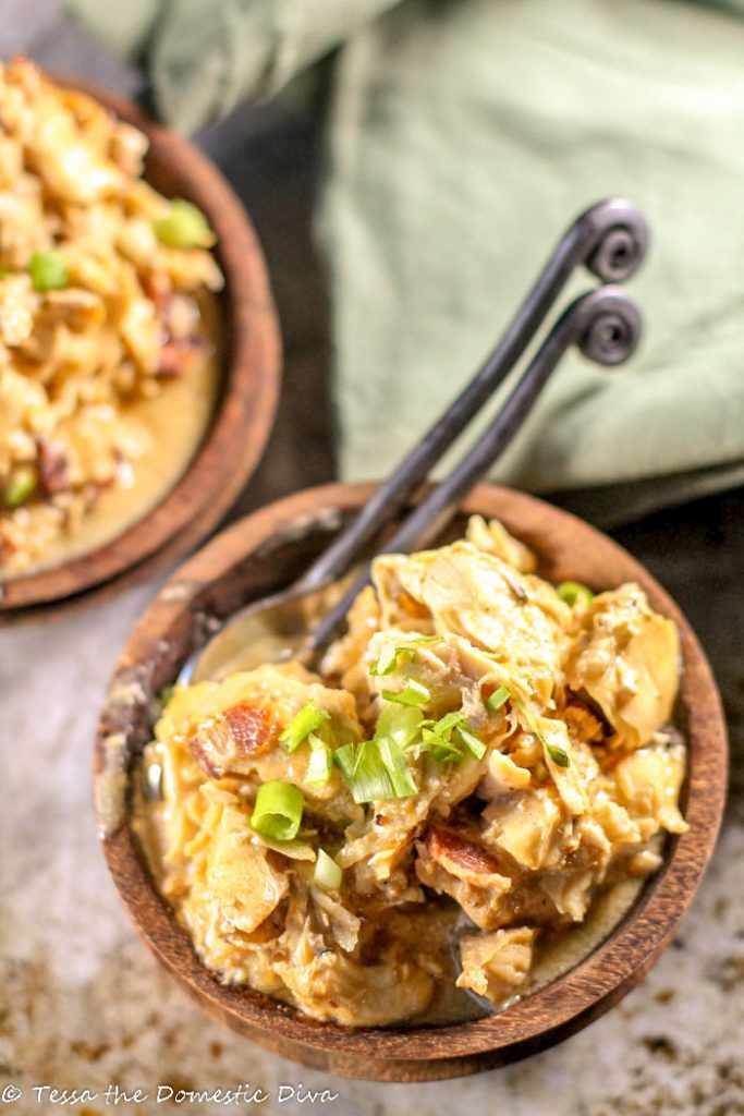 birds eye view of two dark handcarved wooden bowls filled with pulled chicken in a creamy bacon sauce